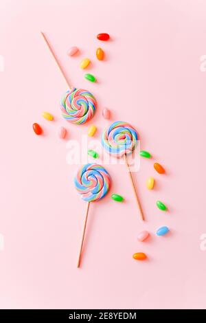 Colorful lollipops swirls on sticks and jelly beans. Striped spiral multicolored candy on pink background, top view Stock Photo