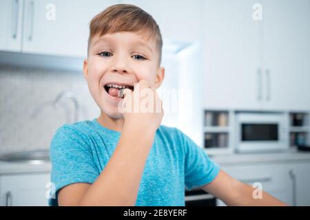 happy kid boy eating or bite chocolate sweets or candies at modern home kitchen Stock Photo