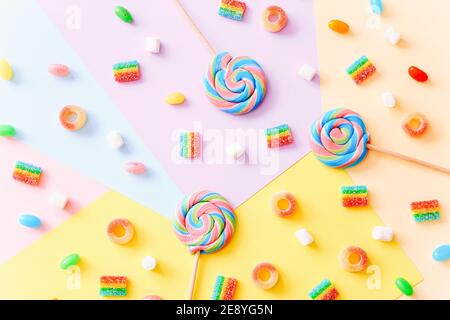 Colorful lollipops swirls on sticks and jelly candies on colorful background, top view Stock Photo