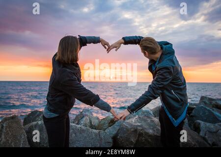 Mesmerizing shot of a loving couple making a heart shape with their arms on the sunset background Stock Photo