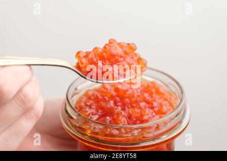 Salmon red caviar in a golden spoon and jar on the white background with copy space.  Stock Photo