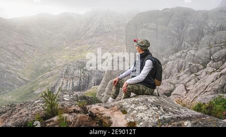 Young woman in sports clothing sitting on rocks enjoying the scenery of Andringitra national park, large stones massif background, during hike to pic Stock Photo