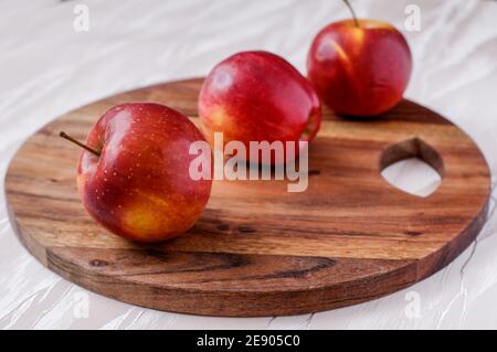 three red ripe apples on a round acacia kitchen board, placed one behind the other Stock Photo