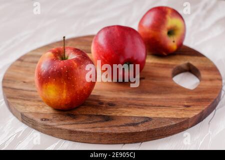 three red ripe apples on a round acacia kitchen board, placed one behind the other Stock Photo