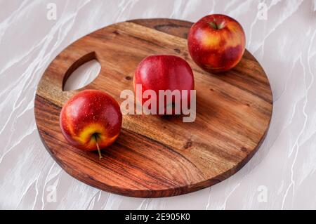 three red ripe apples on a round acacia kitchen board, placed one behind the other Stock Photo