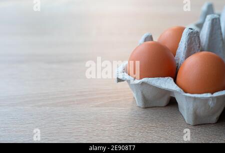 Closeup on carton of three fresh brown free range eggs on a wooden table Stock Photo