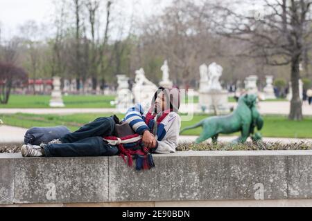 A homeless man lies on a stone curb in the park Stock Photo
