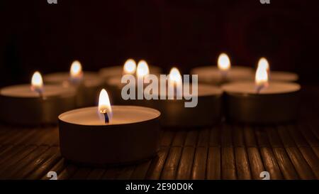 Group of burning candles in the dark with copy space. Romantic concept with tea lights on wooden table Stock Photo