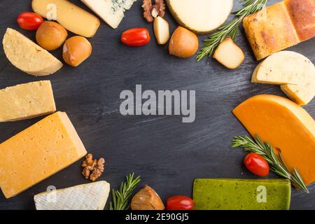 Set of different types of cheese with rosemary and tomatoes in the shape of a frame on a black wooden background. Top view, flat lay, copy space. Stock Photo