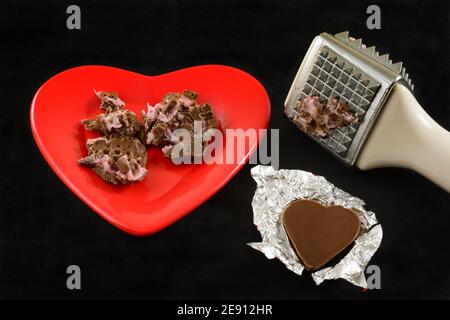 Crushed shredded chocolate heart with pink filling and meat tenderizer mallet and chocolate heart in foil as anti-Valentine symbol of divorce or broke Stock Photo