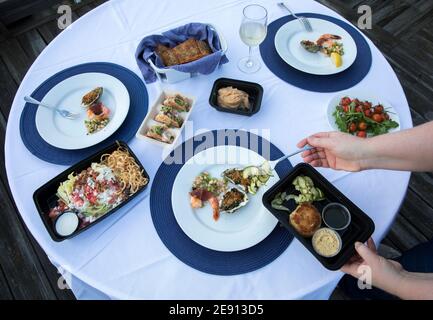 Overhead view of hands serving gourmet takeout food onto white plates Stock Photo