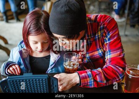 Father and daughter lean in close together at restaurant playing game Stock Photo