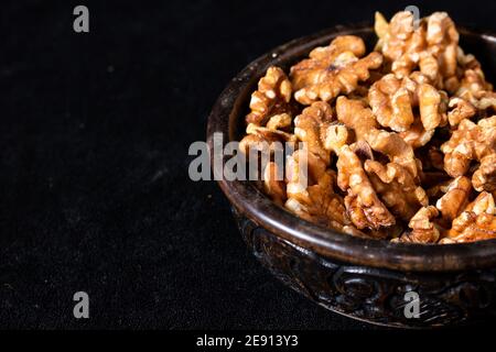 Carved wooden bowl with peeled walnut seeds on a black background. 45 deg. view. Close-up, Space for text.