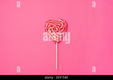 Red heart-shaped lollipop candy isolated on an empty colorful pink background. Symbol of love for Happy Women's, Valentine's Day, Birthday greeting romantic postcard. Flat lay, top view, copy space Stock Photo