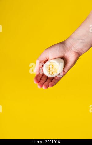 Close up on hand holding boiled egg with yolk in front of yellow background Stock Photo