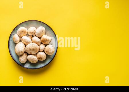 Top view on plate with white common champignon mushrooms on yellow background Stock Photo