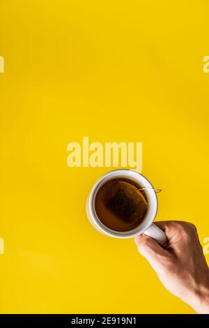 Top view on hands holding cup of tea in front of yellow background Stock Photo