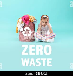 Concerned little girl with clothes in basket on color background. Zero waste concept Stock Photo