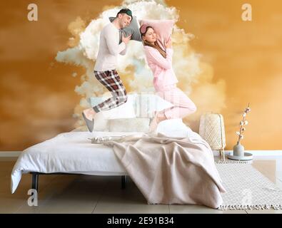 Flying young couple in pajamas and with pillows in interior of comfortable bedroom Stock Photo