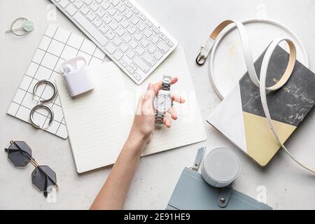 Female hand with stylish wristwatch, gadgets and notebooks on light background Stock Photo