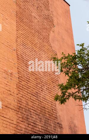 Shabby chic old rusty red color brick wall texture exposed under a deteriorating stucco plaster outer covering Stock Photo