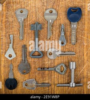 Many assorted old multi-colored metal antique vintage keys of different shapes on wooden scratched table background. Home security concept. Stock Photo