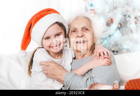 smiling granddaughter in santa hat hugging with grandma at Christmas Stock Photo