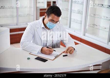 Concentrated eye doctor leaning over a sheet of paper Stock Photo