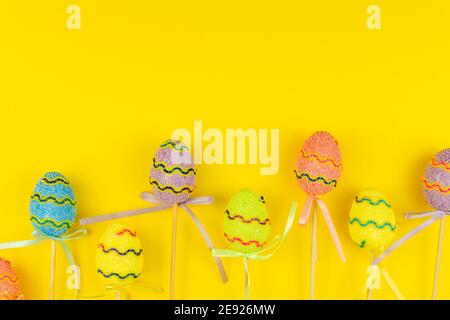 Multicolored Easter eggs on sticks on yellow background. Festive Easter holiday greeting card with copy space. Stock Photo