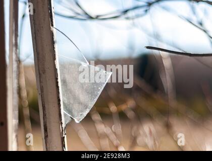 Broken glass following burglary in open window with metal frame sharp edge shard of glass sticking out in derelict building after vandalism Stock Photo