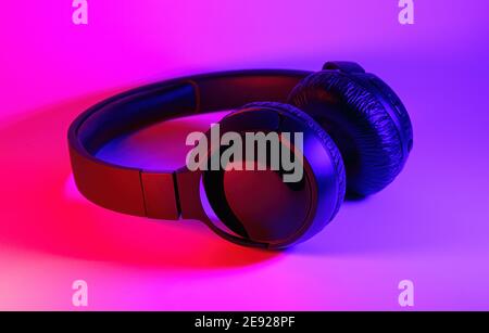 Stylish black wireless headphones lit with colorful neon light on abstract background isolated. Modern technology concept with copy space Stock Photo