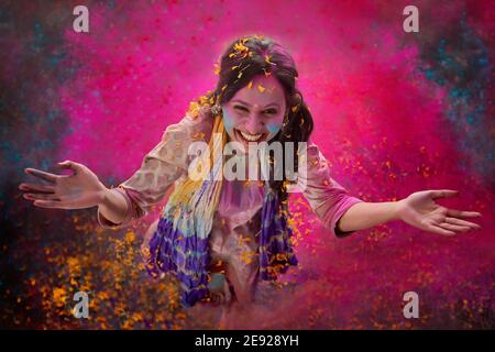 Woman playing Holi with flowers and dancing with gulal on her face Stock Photo