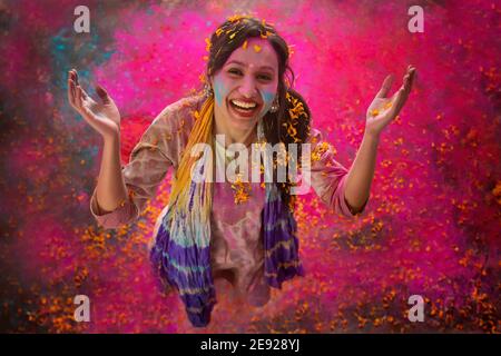 Woman playing Holi with flowers and dancing with gulal on her face Stock Photo