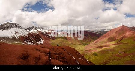 one person sitting at a plateau at red valley, in Peru, enjoying the overview onto the beautiful red and green valley and the snow capped mountains Stock Photo