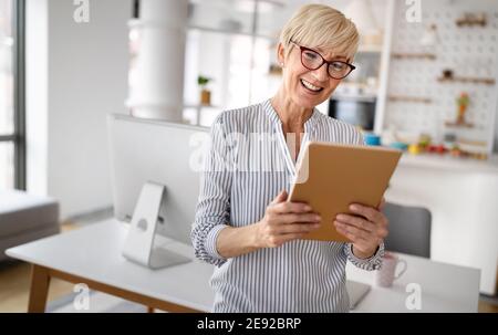 Beautiful happy senior woman using tablet computer at home Stock Photo