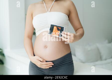 Cheerful pregnant woman holds ultrasound photo at her belly Stock Photo