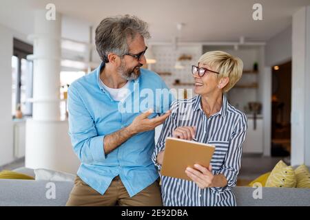 Lovely smiling mature couple having fun while using tablet at home Stock Photo