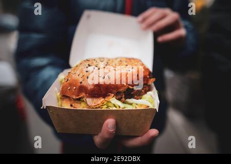 Shallow depth of field (selective focus) with the hands of a young man holding a boxed burger. Stock Photo
