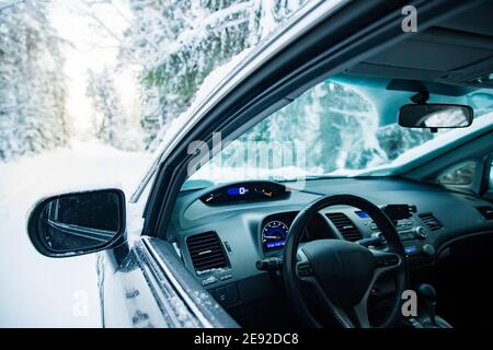 Car covered with snow and ice driving on the winter road. Beautiful landscape of winter forest and snowy country side. Stock Photo
