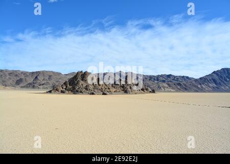 The Grandstand on the Racetrack Playa in the Death Valley National Park, a very dark grey rock surrounded by featureless, light clay sediment Stock Photo