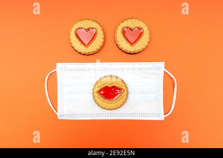 Funny character made of a disposable face mask and cookies with lips and hearts on an orange background. Valentine's day celebration during quarantine Stock Photo