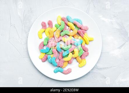 Top view of a white plate full of colored sugar coated gummy worms on a concrete table Stock Photo