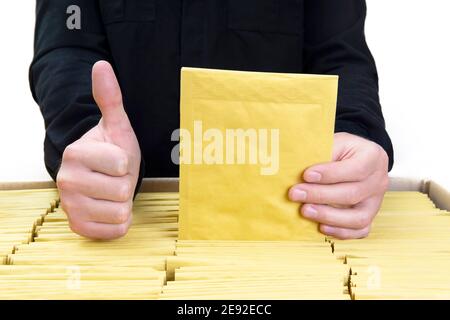 Person in black uniform gets one yellow mail envelope out of a large shipping box with padded bubble envelopes and gives the thumbs up. Stock Photo