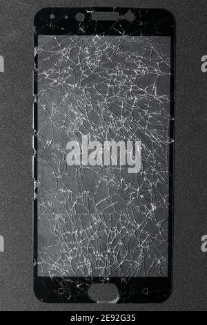 The phone's screen protection film is completely broken and rests on a black-gray background. Stock Photo