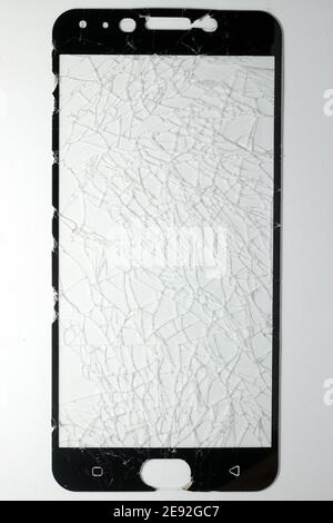 The phone's screen protection film is completely broken and rests on a white background. Stock Photo