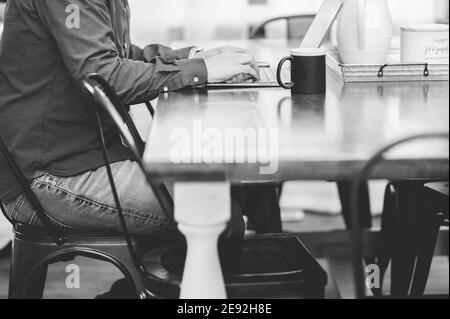 Grayscale shot of a man working with a laptop and drinking a coffee in a cozy cafe Stock Photo