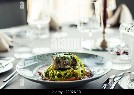 Grilled and flamed ox steak with green herb noodles in a tomato puree at a restaurant Stock Photo