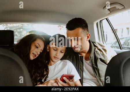 Boy using mobile phone sitting with father and sister in electric car Stock Photo