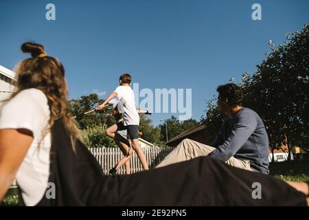 Brother and sister enjoying while parents sitting in back yard on sunny day Stock Photo