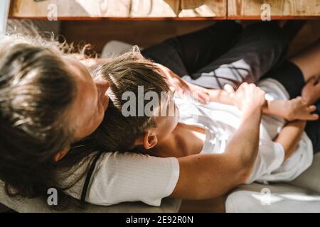 Mother and son lying down on sofa at home during sunny day Stock Photo